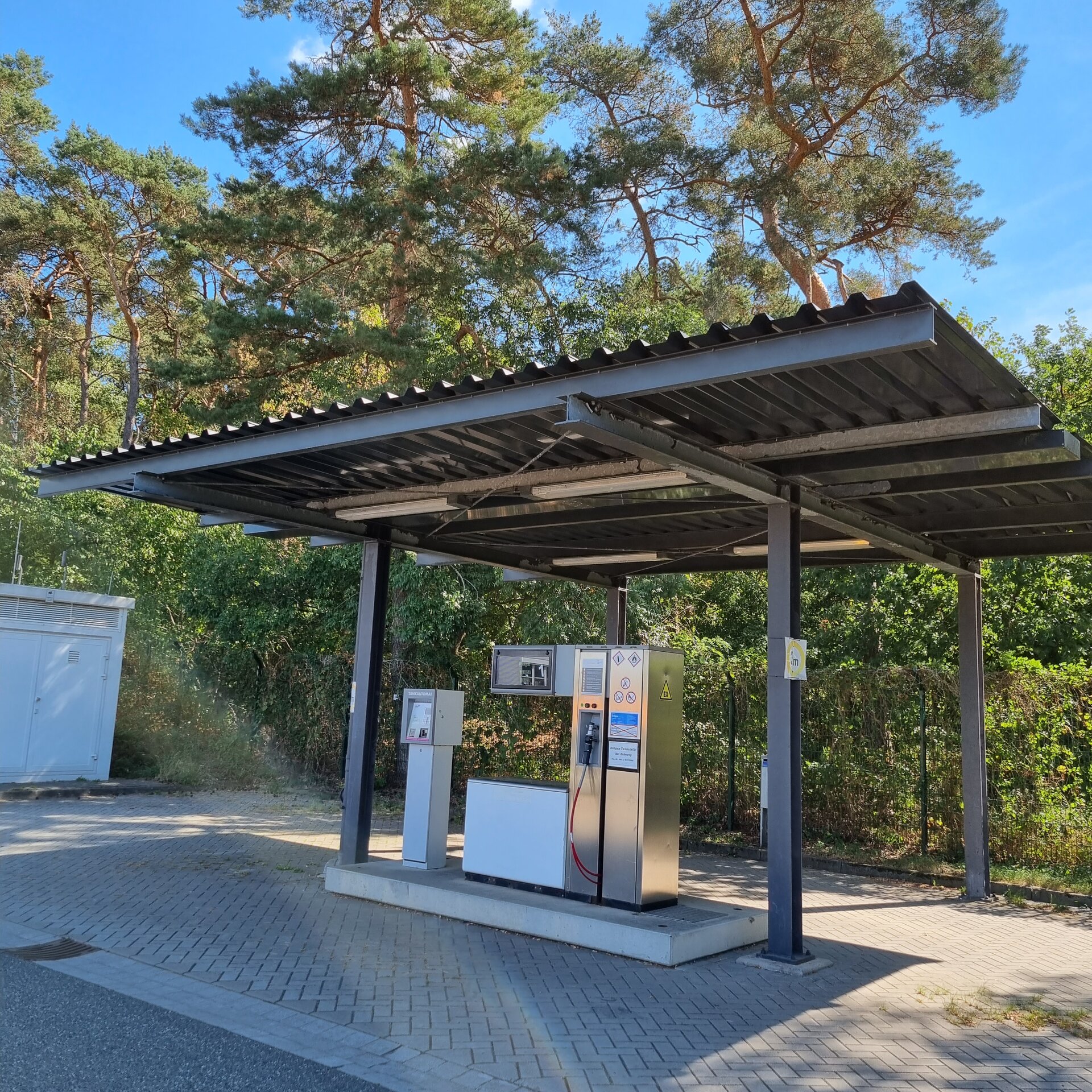 Kleine Tankstelle mit Überdachung im Freien, umgeben von Bäumen.