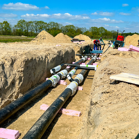 Bauarbeiter verlegen große Rohre in einem Graben auf einer Baustelle.