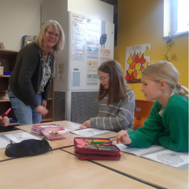 Lehrerin arbeitet mit drei Schülerinnen an einem Tisch im Klassenzimmer.