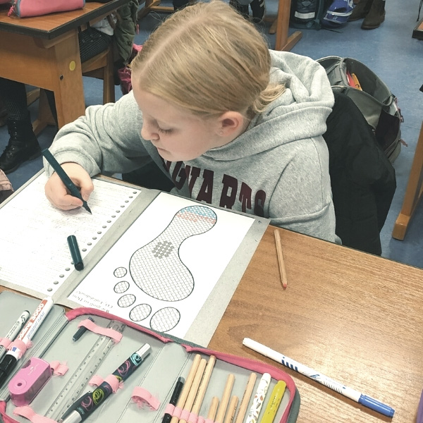 Schülerin malt konzentriert in einem Heft an ihrem Schreibtisch im Klassenzimmer.
