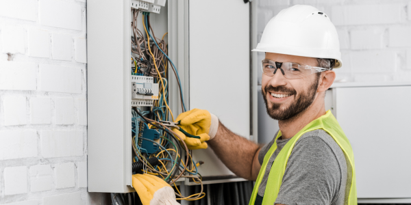 Elektriker mit Schutzhelm und Handschuhen arbeitet an Schaltschrank