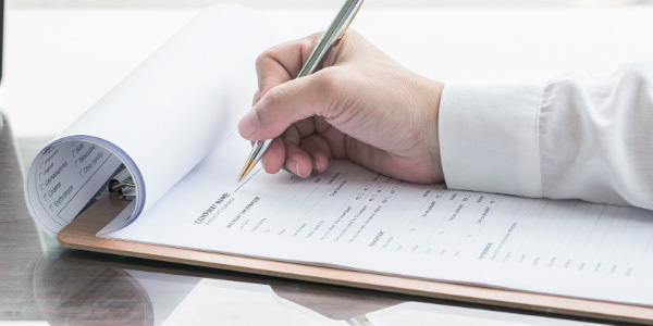 Eine Männerhand mit Stift liegt auf einem Schreibblock