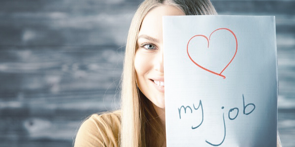 Eine junge Frau hält ein Blatt weißes Papier halb vor ihr Gesicht - zu sehen ist dort ein rotes Herz und das Wort Job.