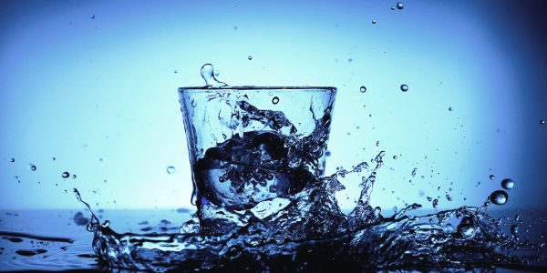Ein Glas mit Wasser vor blauem Hintergrund - Wassertropfen spritzen hoch