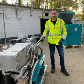 Mann in gelber Warnweste steht neben einer großen Maschine auf einer Baustelle.