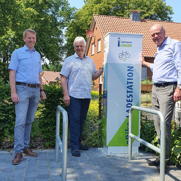 Drei Männer stehen neben einer Ladestation der Stadtwerke Lingen im Freien.