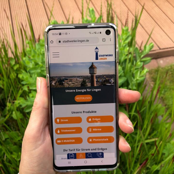 Eine linke Hand hält ein Mobilfunktelefon, auf dem die Mobile Version einer Website zu sehen ist.