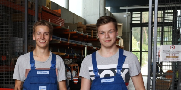 Zwei junge Männer in blauen Arbeitsanzügen in einem Lager